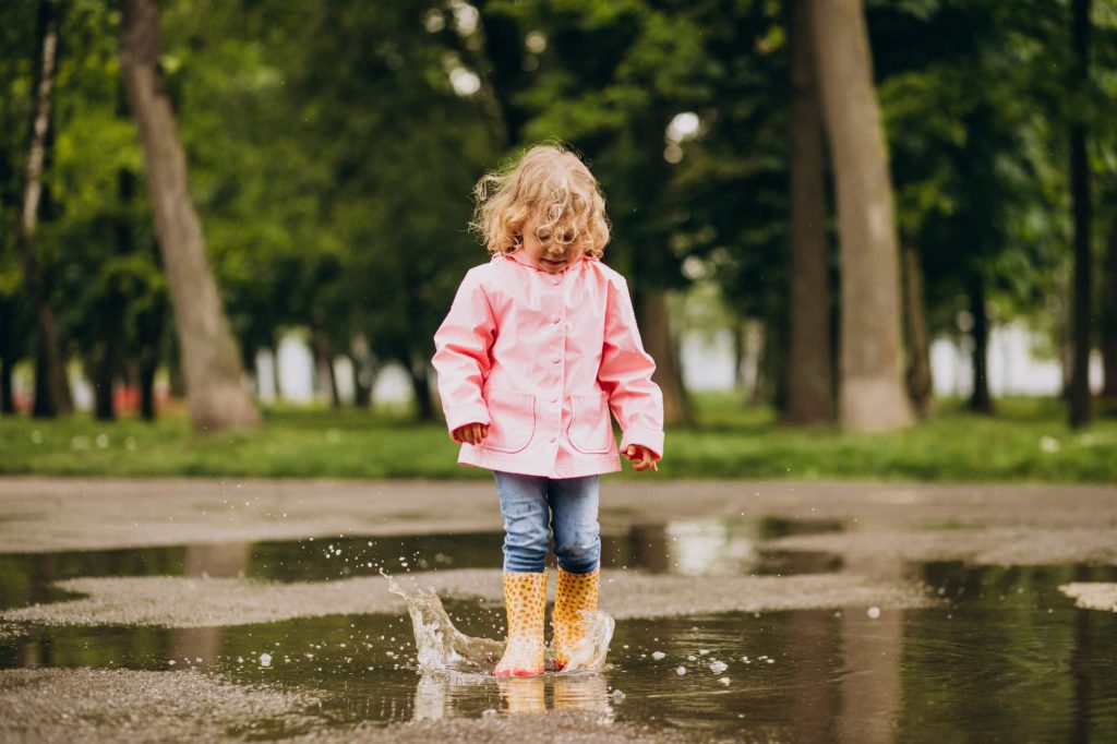 cute little girl jumping into puddle rainy weather